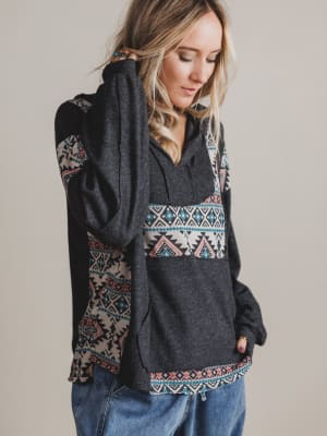 Woman wearing a dark gray hoodie with colorful geometric patterns on a plain background