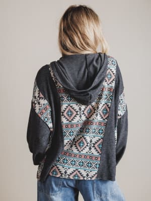 Person wearing a dark gray hoodie with a patterned back on a plain background