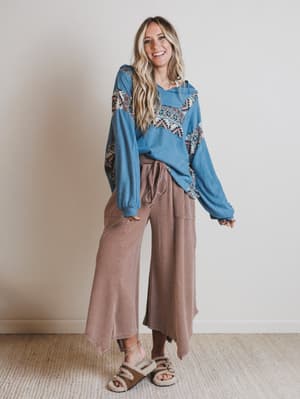 Woman wearing a blue patterned top and brown pants against a plain background