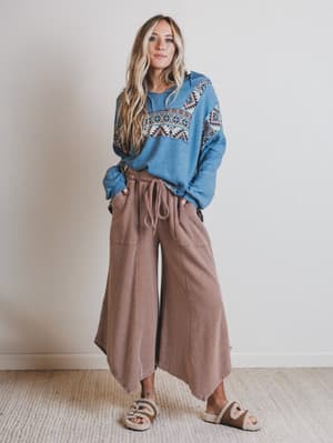 Woman wearing a blue sweater with patterned design and brown wide-leg pants against a plain background