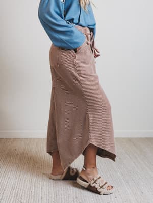 Person wearing a blue sweater and brown striped pants on a plain background