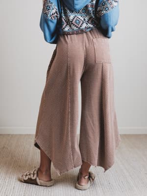 Person wearing a patterned top, blue jacket, and brown wide-leg pants on a neutral background