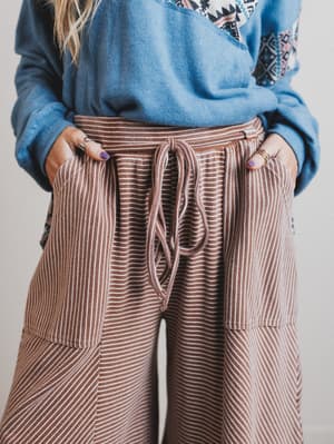 Person wearing a blue sweater and brown striped pants against a neutral background