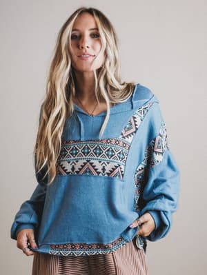 Woman wearing a blue hoodie with a patterned design on a plain background