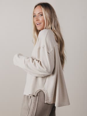 Woman wearing a beige sweater and pants against a plain background