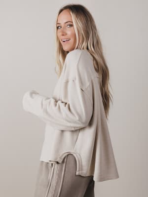Woman wearing a beige sweater and pants against a plain background