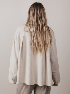 Person wearing a beige jacket and pants against a plain background