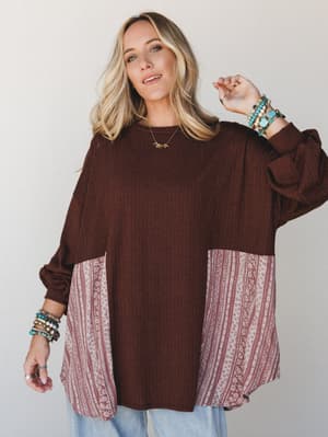 An oversized ribbed top in deep chocolate brown with contrast patchwork panels in a dusty rose floral-stripe print, styled with layered turquoise bead bracelets and light wash jeans for an effortlessly collected, everyday boho feel.