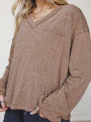 A relaxed, heathered brown long-sleeve top with a chest pocket and easy v-neck, styled with dark jeans and layered gold necklaces — the kind of top that does a lot of quiet work in a wardrobe.