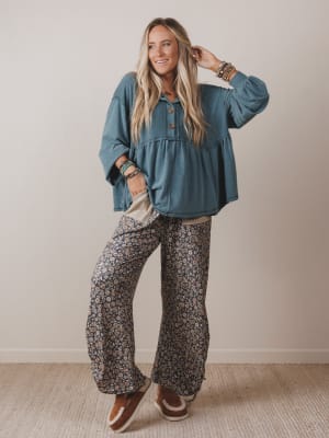 Woman wearing a blue top and patterned pants against a plain background