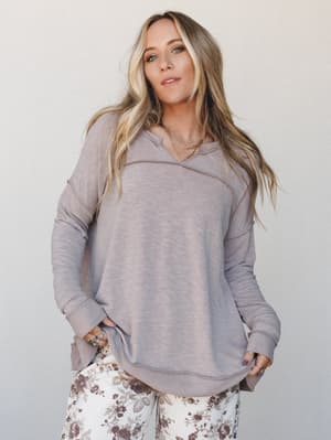 A relaxed, lived-in pullover sweater in warm taupe-brown worn over floral wide-leg pants — the kind of outfit that makes a coffee run feel intentional.