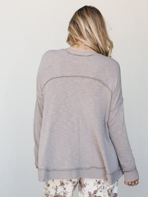 Shot from behind, a relaxed pullover sweater in muted taupe pairs with floral printed pants — the whole look reads like a slow Saturday morning with nowhere to be.