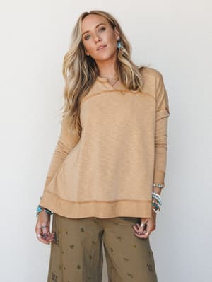 A relaxed, lived-in pullover in warm camel-mustard is paired with olive floral wide-leg pants and layered turquoise jewelry — the kind of outfit that looks effortless but is clearly very thought out.