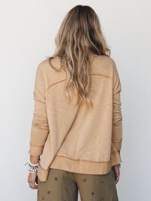 Shot from the back, a model in a warm camel pullover with visible contrast stitching and ribbed trim is paired with olive floral wide-leg pants — the kind of effortless, lived-in outfit that makes you want to stay in it all day.