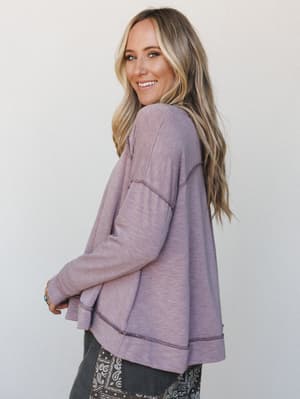 A relaxed, lived-in pullover in a soft mauve-lavender shot from a three-quarter back angle — the kind of top that earns 'where'd you get that?' at school pickup.