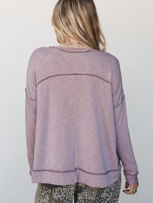 A back-facing shot of a relaxed, mauve pullover with exposed seam detailing and a lived-in heathered texture, styled with paisley pants for an effortlessly cozy everyday look.