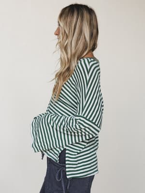 A side-profile shot of a striped bell sleeve top in forest green and white, styled with dark charcoal pants — the kind of top that makes a Tuesday feel like it has a little more going on.