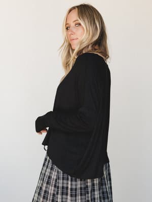 A relaxed black long-sleeve top paired with a black-and-white plaid skirt, shot from a side profile angle — easy, collected, and the kind of outfit that looks effortless without trying.
