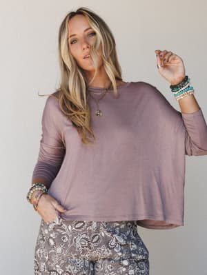 A relaxed, oversized long sleeve crop top in a washed dusty mauve pairs effortlessly with floral printed wide-leg pants, styled with layers of beaded bracelets and a gold pendant necklace for that collected, lived-in boho feel.