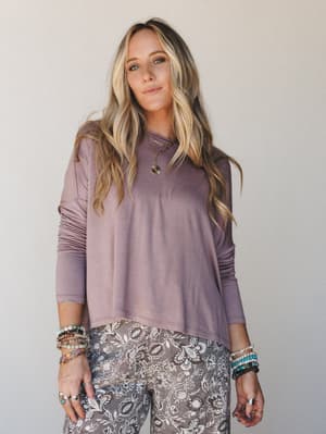 A relaxed long sleeve top in muted mauve paired with floral printed pants, styled with layered gold necklaces and a stack of boho bracelets — the kind of effortless outfit that looks like you tried just enough.