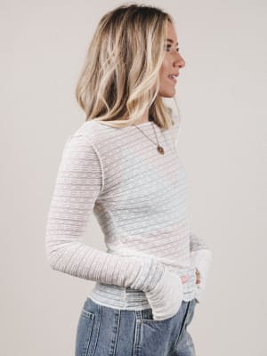 Woman wearing a light gray sweater and blue jeans against a plain background