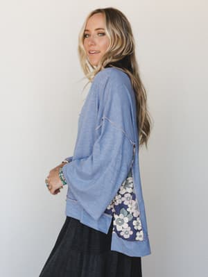 A relaxed, side-profile shot of a flowy periwinkle blue top with a surprise floral panel peeking out from the back hem — the kind of top that looks effortless but clearly has something going on.