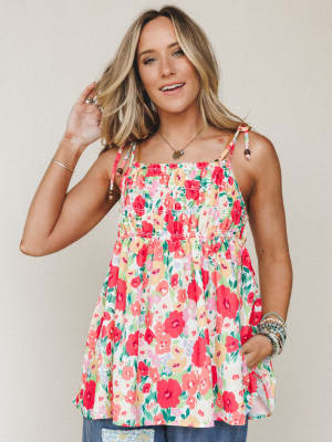 A flowy floral babydoll top in a vibrant red poppy print styled with stacked bracelets and a delicate pendant necklace — the kind of top that makes a Tuesday feel like a garden party.
