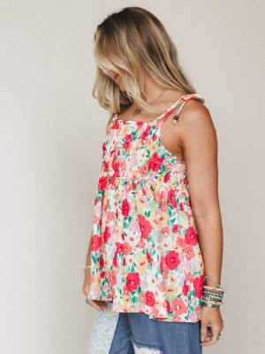 A breezy floral tank top with smocked detailing and a flowy babydoll silhouette, styled with distressed jeans and stacked bracelets — the kind of top that makes a regular Tuesday feel like a garden party.