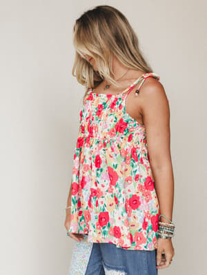A breezy floral tank top with smocked detailing and a flowy babydoll silhouette, styled with distressed jeans and stacked bracelets — the kind of top that makes a regular Tuesday feel like a garden party.
