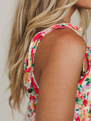 A close-up shoulder shot of a floral top with knotted tie straps and wooden button details — the kind of summery, feel-good piece that looks like it belongs on a patio somewhere warm.
