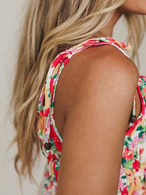 A close-up shoulder shot of a floral top with knotted tie straps and wooden button details — the kind of summery, feel-good piece that looks like it belongs on a patio somewhere warm.
