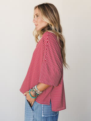 A side profile shot of a model in a relaxed red and white striped boxy top paired with printed wide-leg jeans and a stack of colorful beaded bracelets — effortless and a little nostalgic, like a weekend that has nowhere to be.