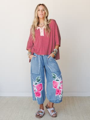 A relaxed, expressive outfit pairing an oversized marsala striped henley top with wide-leg floral appliqué pants — the kind of look that feels effortless but clearly has a point of view.