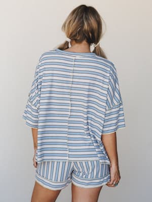 Shot from behind, a model wears a matching striped oversized top and shorts set in soft blue, cream, and black — relaxed and easy, like something you'd reach for on a slow Saturday morning that somehow looks completely put-together.