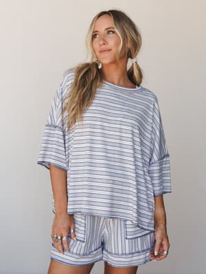 A relaxed striped matching set — oversized top and shorts in a soft blue and white stripe — styled with layered rings and pearl hair ties for that effortless, I-just-threw-this-on-and-it-works energy.