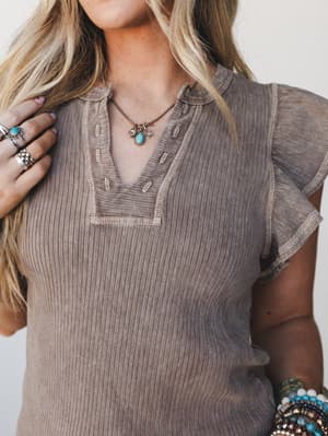A close-up model shot of a washed brown ribbed tee with flutter sleeves and a notched v-neckline, styled with layered turquoise jewelry and stacked beaded bracelets for that effortless boho-everyday feel.