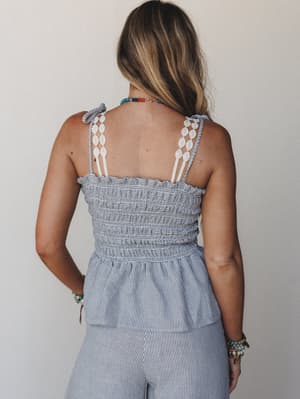 A back-facing shot of a smocked stripe camisole top paired with matching wide-leg stripe pants — the crochet trim shoulder straps and colorful beaded jewelry give it an easy, sun-worn summer feel.