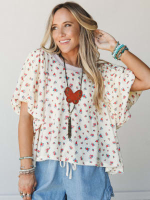 A breezy ditsy floral top with wide ruffle sleeves is styled with chambray shorts and layered boho accessories — the kind of outfit that feels effortless but clearly had a moment of intention behind it.