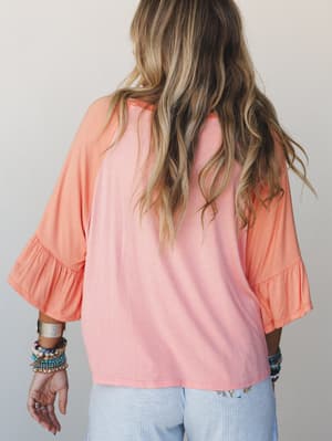 Shot from the back, a relaxed bell sleeve top in a soft peach-to-tangerine ombre pairs with light blue wide-leg pants — the stacked bracelets and wavy hair do all the right boho things.