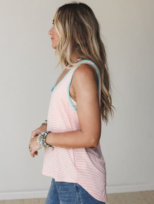 A side-profile shot of a model in a coral striped tank with aqua trim details, stacked beaded bracelets, and relaxed denim — the kind of effortless warm-weather outfit you reach for without thinking twice.