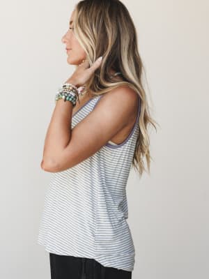 A relaxed striped tank with a soft lavender trim detail, styled with stacked beaded bracelets and dark jeans — the kind of effortless layering piece that just makes getting dressed easier.