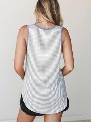 Back view of a striped tank with a periwinkle contrast neckline and curved hem, styled with dark shorts and layered beaded jewelry — effortless and easy in the best way.