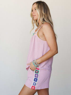 A breezy orchid pink tank and shorts set with colorful granny square crochet trim details, styled with layered beaded bracelets and a delicate necklace — effortlessly warm-weather and full of personality.