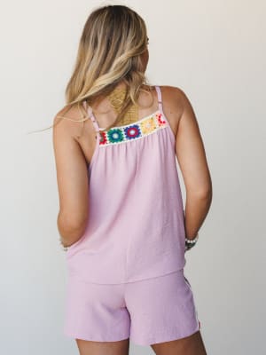 A back-facing model in a matching orchid pink tank and shorts set, the top's standout detail being a colorful granny square crochet trim across the upper back — playful, summery, and the kind of outfit that makes a Saturday feel intentional.