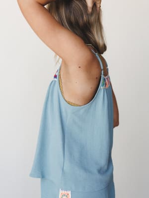 A breezy, flowy camisole tank shot from the back, showing off an open low back with a gold trim neckline and colorful crochet patchwork detail at the shoulders — easy, expressive, and made for warm days.