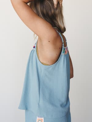 A breezy, flowy camisole tank shot from the back, showing off an open low back with a gold trim neckline and colorful crochet patchwork detail at the shoulders — easy, expressive, and made for warm days.