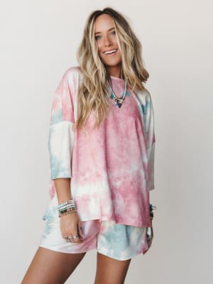 A tie-dye matching set in cotton candy pink and soft sage — oversized tee paired with biker-length shorts, styled with layered beaded bracelets and a charm necklace for that effortless, feel-good energy.