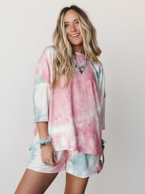 A tie-dye matching set in cotton candy pink and soft sage — oversized tee paired with biker-length shorts, styled with layered beaded bracelets and a charm necklace for that effortless, feel-good energy.