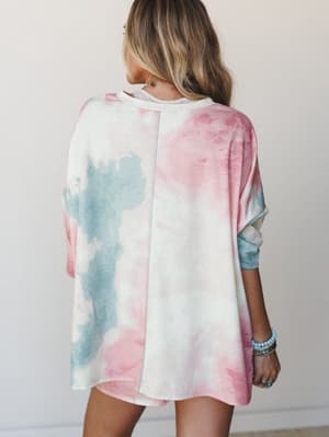 Back view of an oversized tie-dye top in cotton candy pink and dusty blue, styled with stacked turquoise and silver bracelets — the kind of piece that looks equally at home on a coffee run or a lazy beach day.