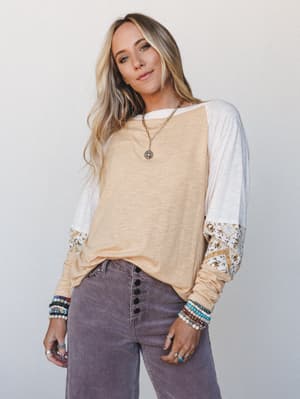 A relaxed long-sleeve colorblock top in warm mango and white with printed cuff detail, styled with wide-leg corduroy pants and layered boho jewelry for an effortlessly put-together everyday look.